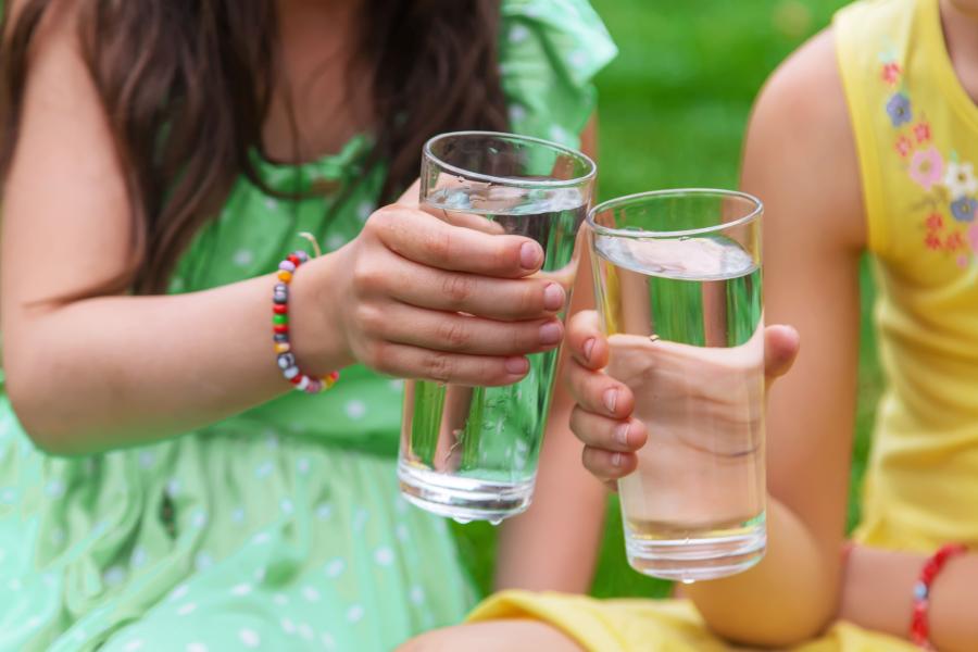 Two young girls holding glasses full of water cheers