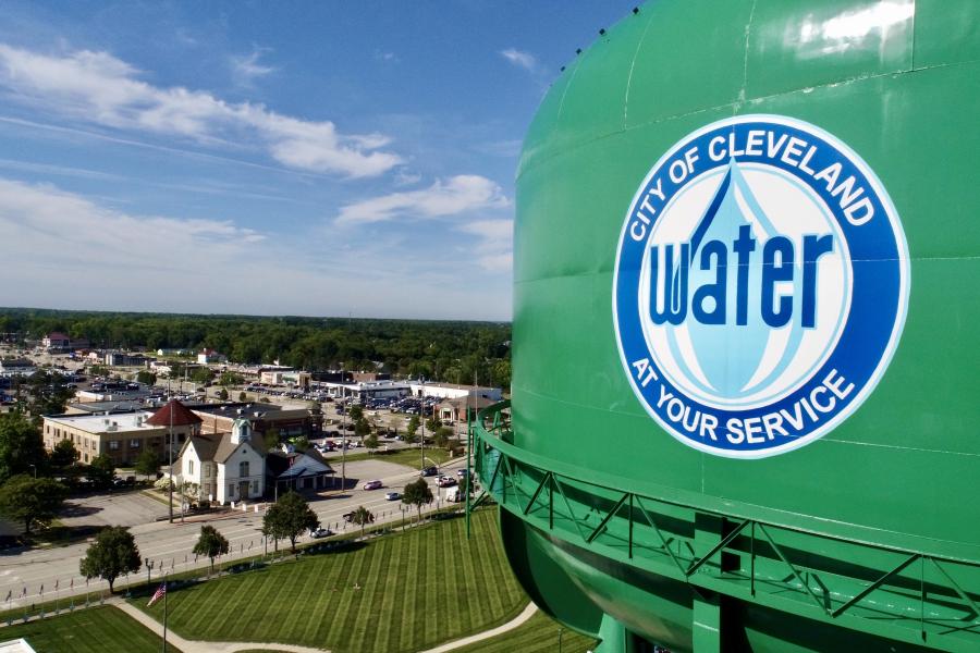 A green water tower with a Cleveland Water logo stands in the right foreground with a suburban city behind it