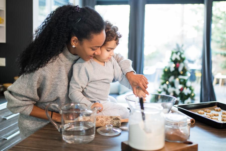 A mom and her young son are baking in the kitchen. Behind them is a Christmas tree.