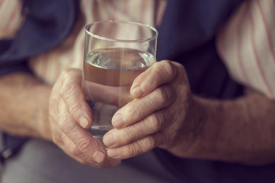 Close up of the hands of an elderly person holding a glass of water
