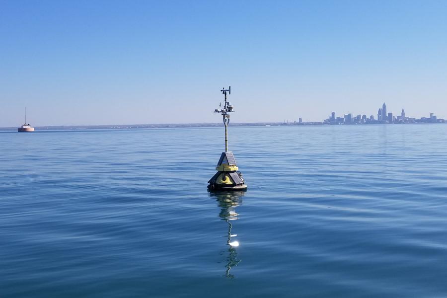 A yellow buoy floats in Lake Erie with the downtown Cleveland skyline in the distance