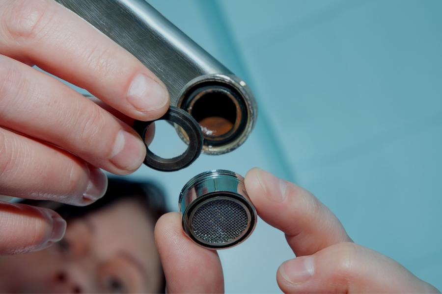 Close up of a person removing an aerator from the end of a faucet