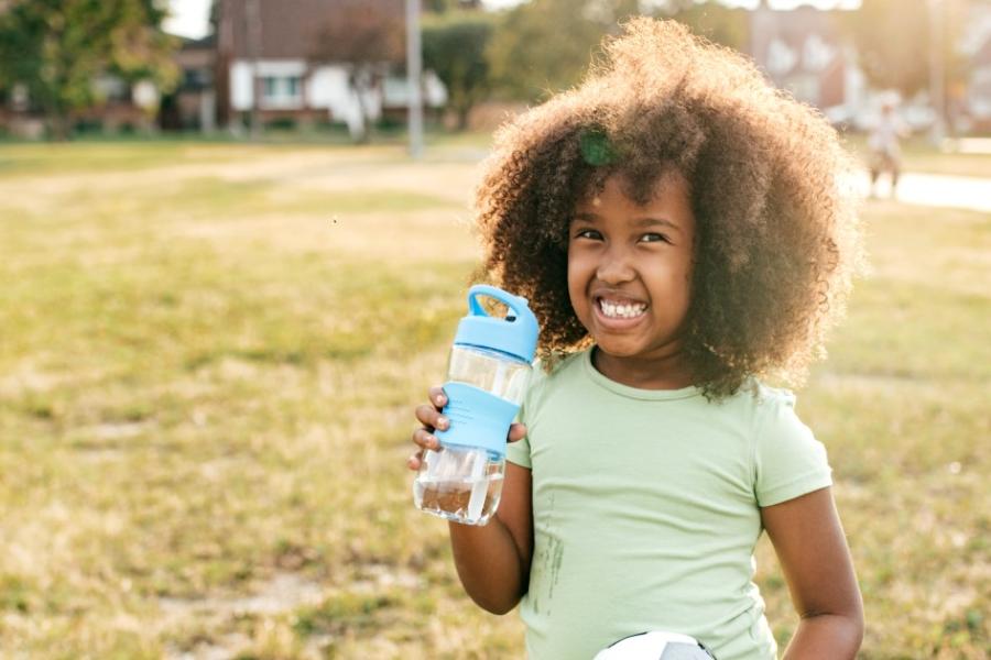 A young girl smiles while holding a water bottle and playing outside