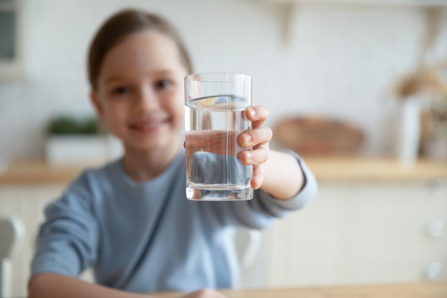 A young girl smiles while holding a glass of water