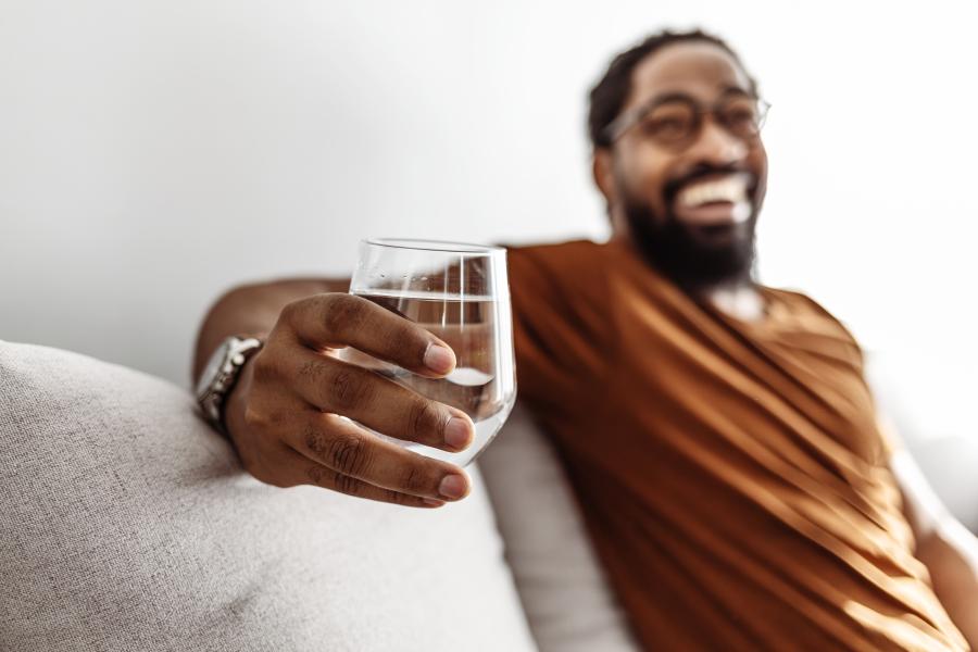 A man hold a glass of water while sitting on a couch smiling