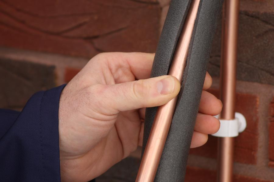 A man places foam insulation around a copper pipe
