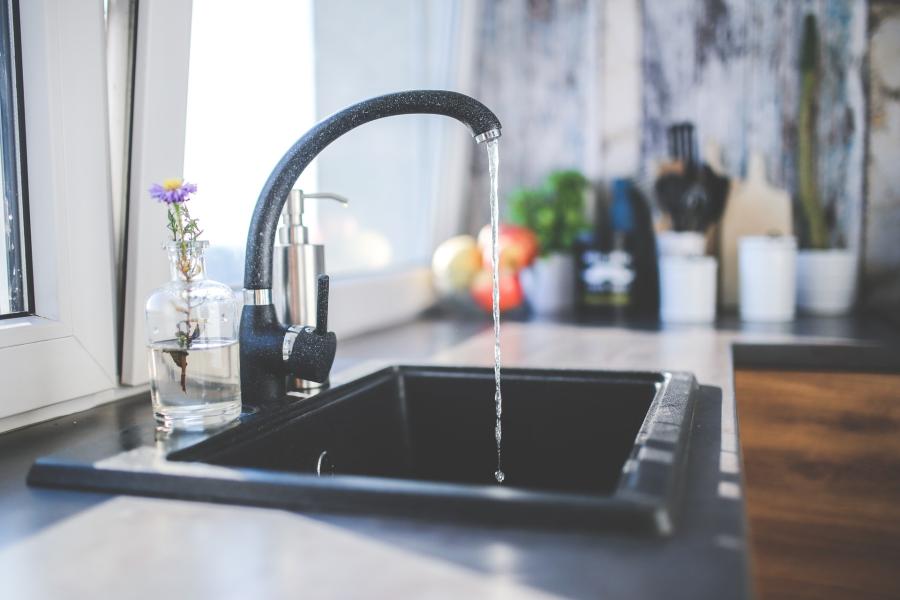 A black kitchen sink and faucet with water running from it