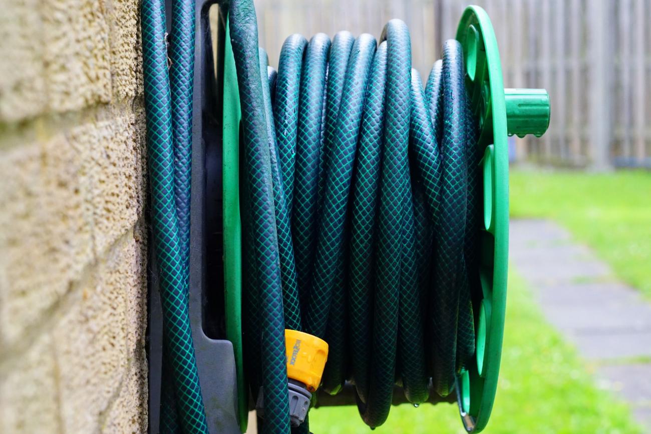 A green garden hose coiled onto a hose reel mounted on the side of a house