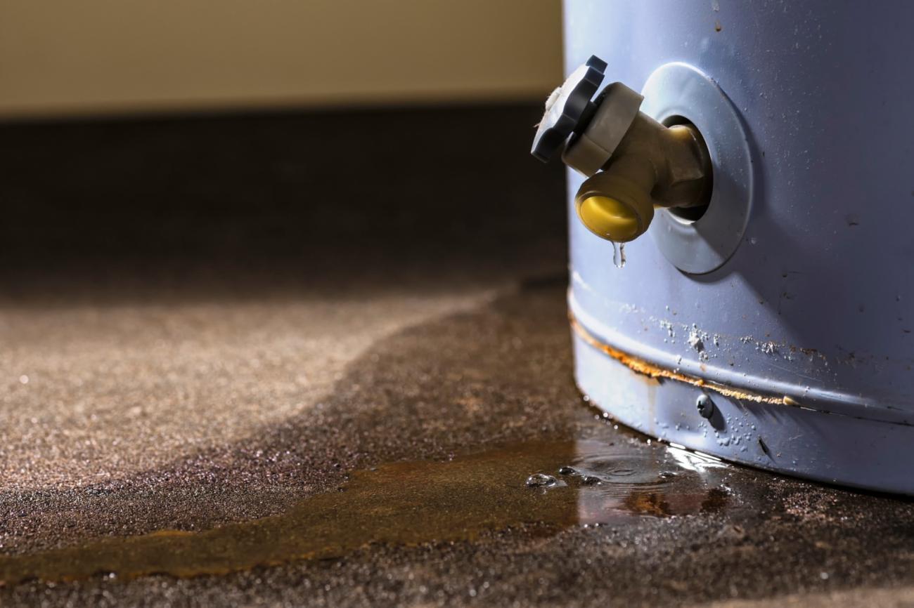A valve at the bottom of a water heater dripping onto a basement floor