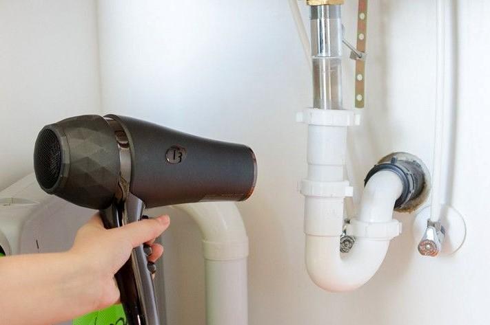 Woman using a blow dryer to thaw a frozen bathroom pipe