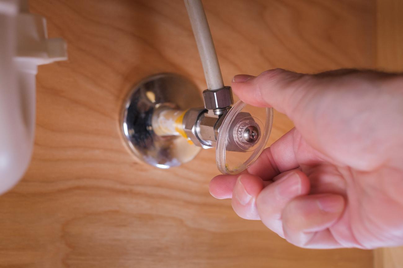 A hand turning a water valve under a bathroom sink