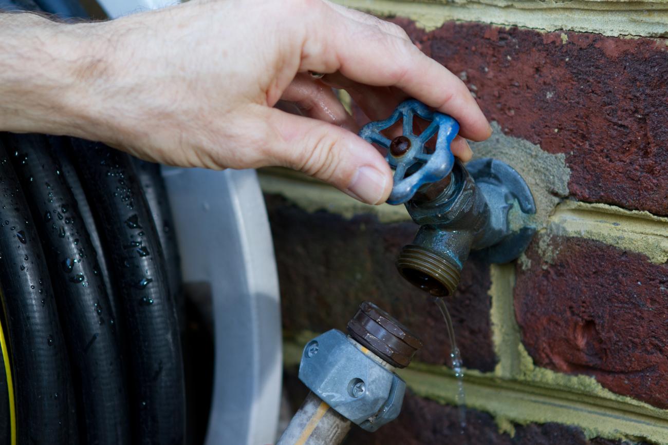 A man's hand disconnects a hose from a spigot