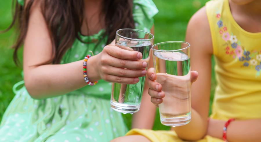 Two young girls holding glasses full of water cheers