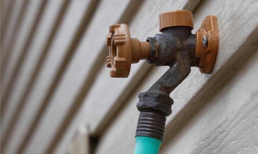 An outdoor spigot on the side of a house with a hose attached