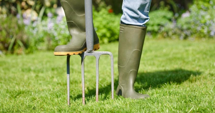 A person in rubber boots uses a garden tool on a lawn