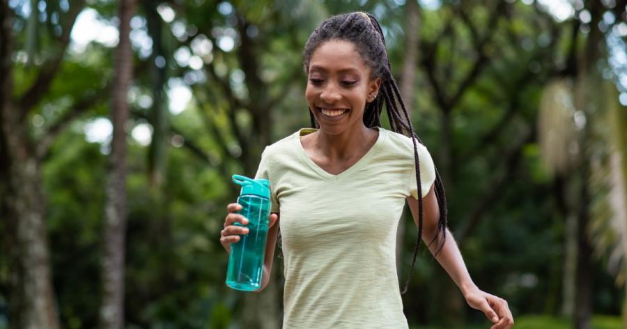 A smiling woman jogs while holding a water bottle