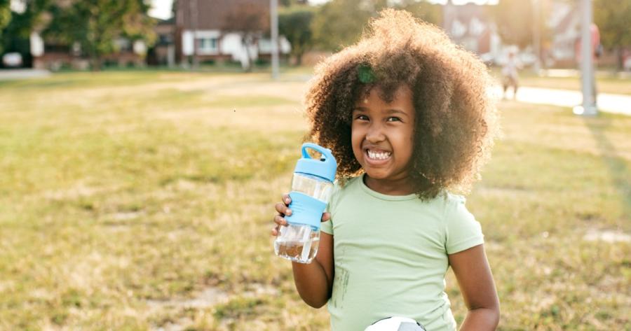 A young girl smiles while holding a water bottle and playing outside
